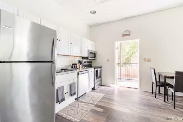 kitchen featuring white cabinets, appliances with stainless steel finishes, light stone counters, and light hardwood / wood-style flooring