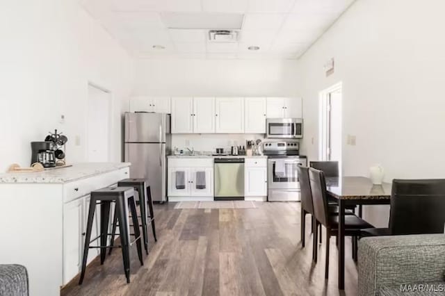 kitchen featuring white cabinets, appliances with stainless steel finishes, a kitchen breakfast bar, and hardwood / wood-style floors