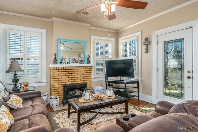 living room with wood-type flooring, a textured ceiling, ceiling fan, crown molding, and a brick fireplace