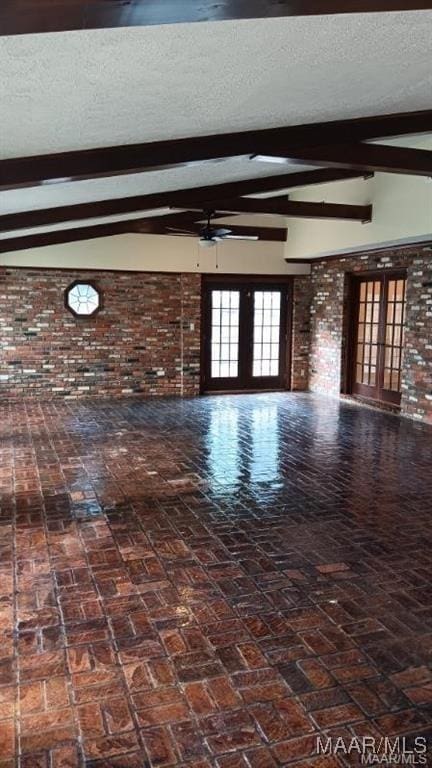 unfurnished living room with french doors, brick wall, a textured ceiling, and beam ceiling