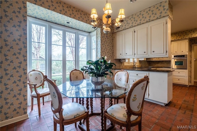 dining room featuring wallpapered walls, a notable chandelier, baseboards, and brick floor