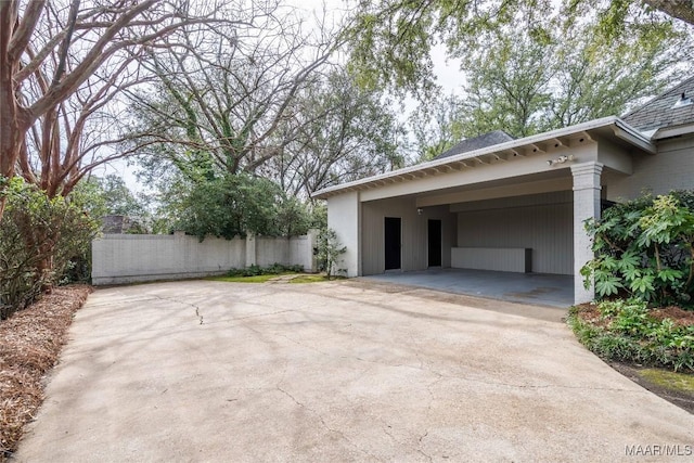 garage with fence, concrete driveway, and an attached carport