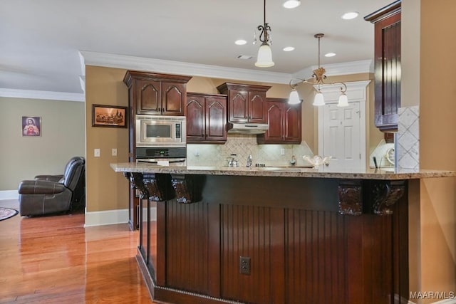 kitchen featuring stainless steel microwave, wall oven, light stone countertops, ornamental molding, and hanging light fixtures
