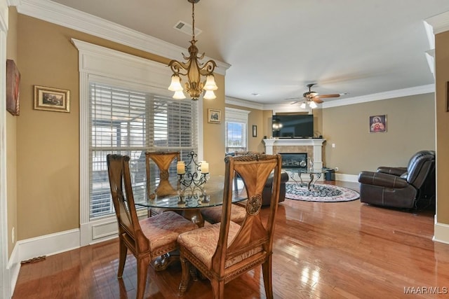 dining space with a ceiling fan, wood finished floors, crown molding, baseboards, and a tiled fireplace
