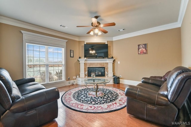 living area with ceiling fan, ornamental molding, wood finished floors, baseboards, and a tiled fireplace