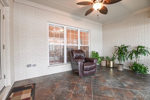 sitting room with brick wall, a ceiling fan, stone finish floors, and ornamental molding