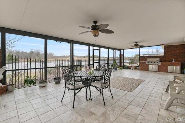 sunroom with exterior kitchen, a water view, a ceiling fan, and tile patterned flooring