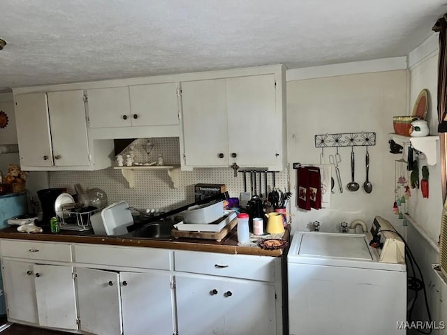 kitchen featuring dark countertops, washer / clothes dryer, white cabinets, and backsplash