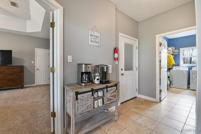 entryway featuring light tile patterned floors, baseboards, visible vents, a textured ceiling, and washer and dryer