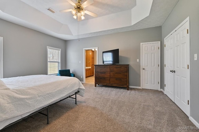 bedroom with a textured ceiling, light colored carpet, visible vents, baseboards, and a raised ceiling