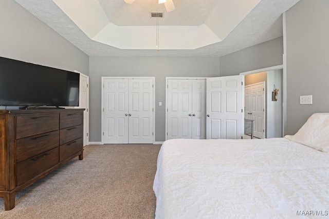 bedroom featuring two closets, a raised ceiling, light colored carpet, visible vents, and a textured ceiling