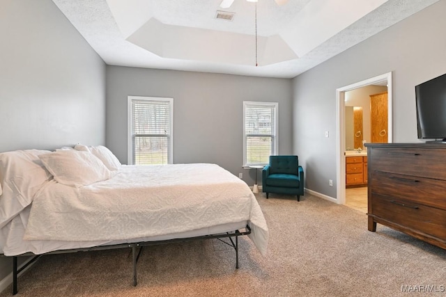 bedroom featuring connected bathroom, light colored carpet, visible vents, baseboards, and a tray ceiling