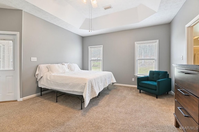 bedroom featuring light carpet, a tray ceiling, visible vents, and baseboards