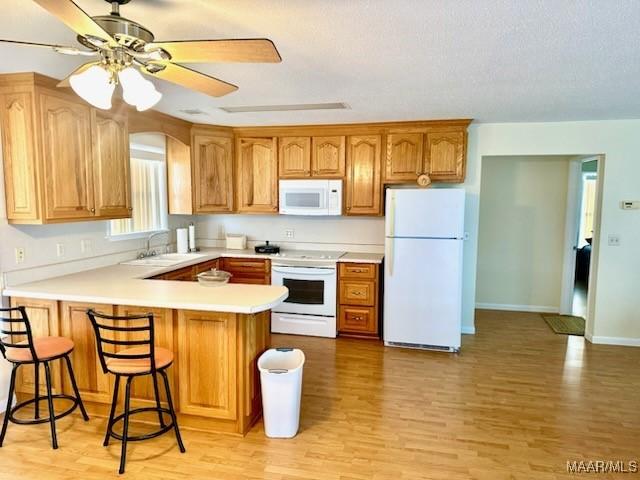 kitchen featuring a breakfast bar, light countertops, a sink, white appliances, and a peninsula