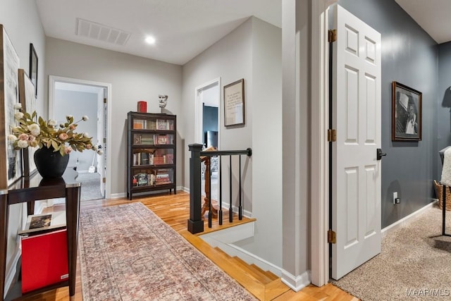 hallway with an upstairs landing, wood finished floors, visible vents, and baseboards