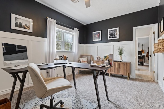 office area with ceiling fan, a decorative wall, a wainscoted wall, visible vents, and carpet