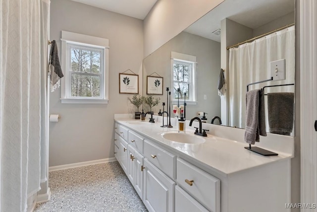 full bath with a sink, baseboards, and double vanity