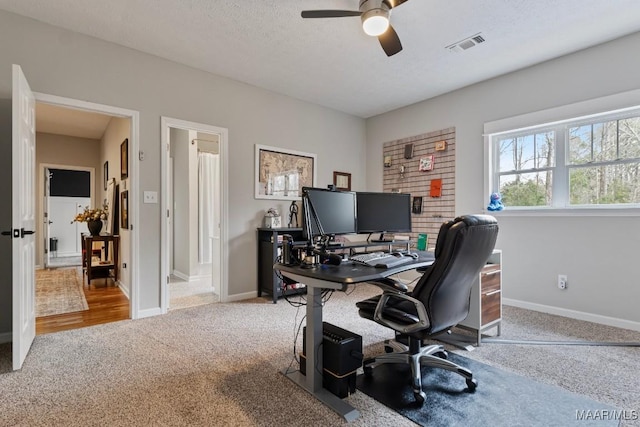 office with light colored carpet, visible vents, a ceiling fan, a textured ceiling, and baseboards