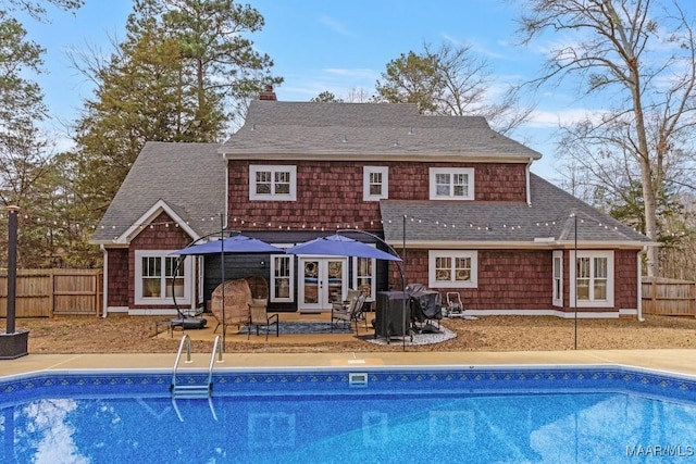 rear view of property featuring a shingled roof, a chimney, fence, and a fenced in pool