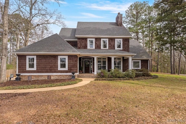 shingle-style home with covered porch, roof with shingles, a chimney, and a front yard