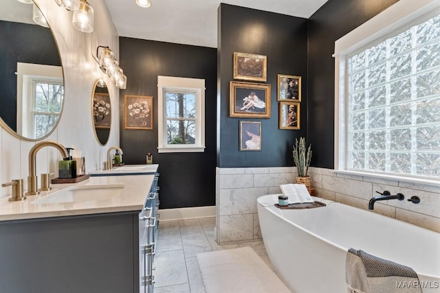 full bath with marble finish floor, double vanity, a sink, and a healthy amount of sunlight