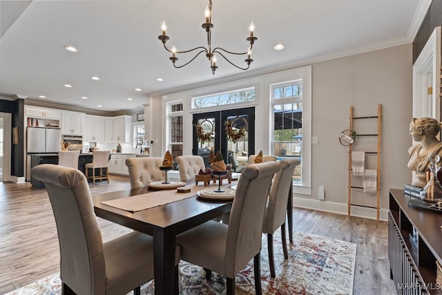 dining area with ornamental molding, a notable chandelier, plenty of natural light, and light wood finished floors