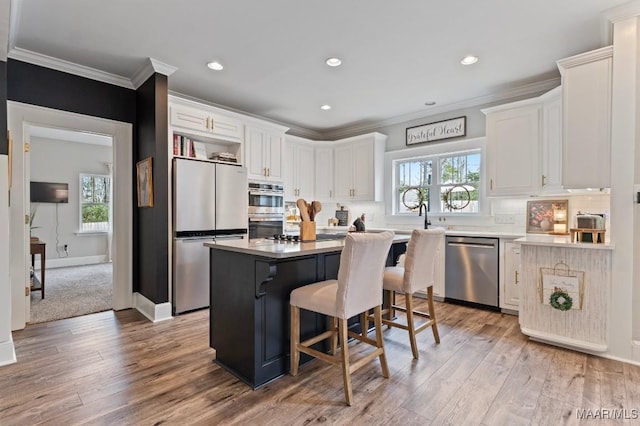 kitchen featuring stainless steel appliances, a kitchen island, white cabinets, ornamental molding, and tasteful backsplash