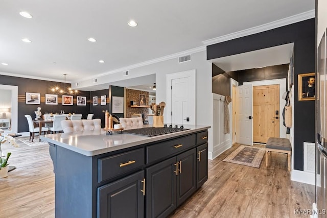 kitchen featuring visible vents, ornamental molding, a center island, hanging light fixtures, and light wood-style floors