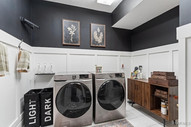 clothes washing area featuring laundry area, light tile patterned floors, a decorative wall, and washing machine and clothes dryer