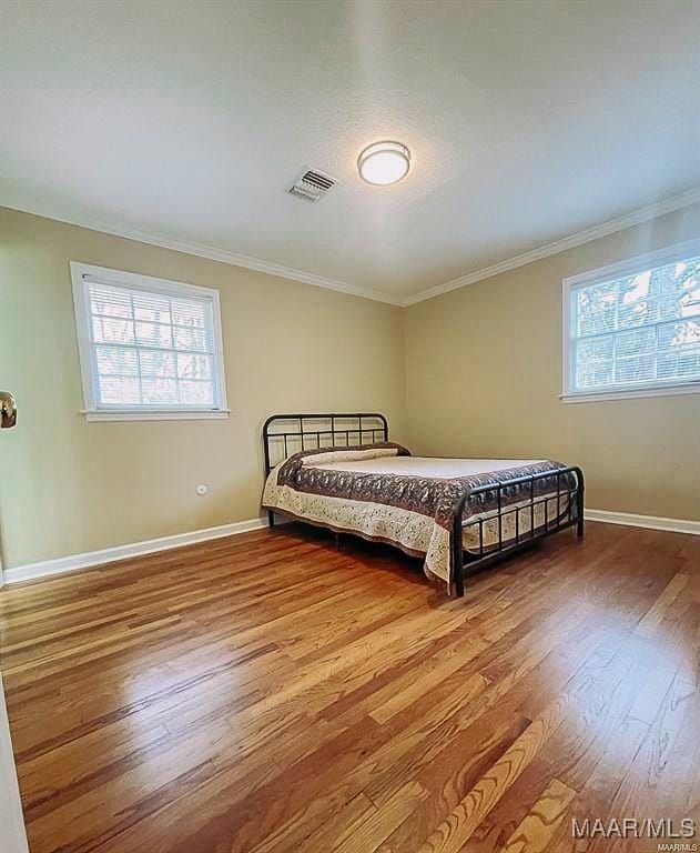 bedroom featuring ornamental molding, visible vents, baseboards, and wood finished floors