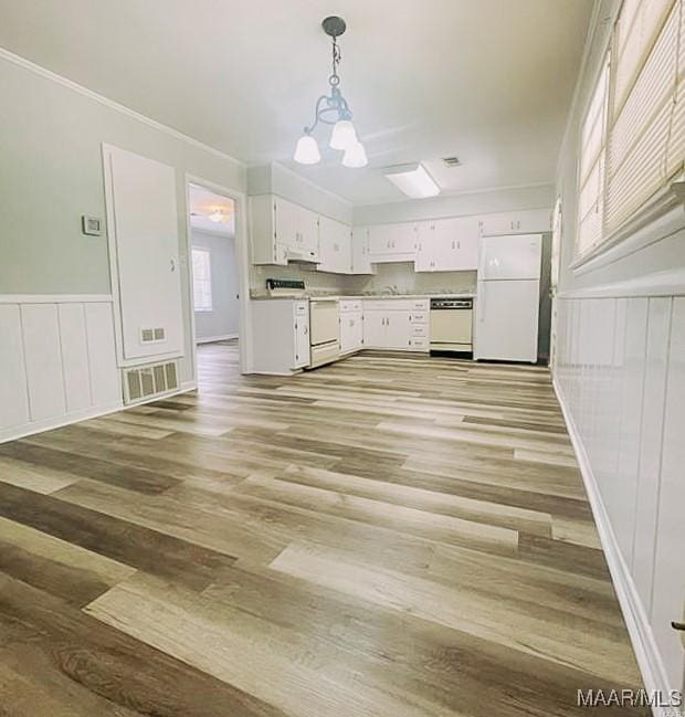 kitchen with white appliances, visible vents, wainscoting, hanging light fixtures, and white cabinetry