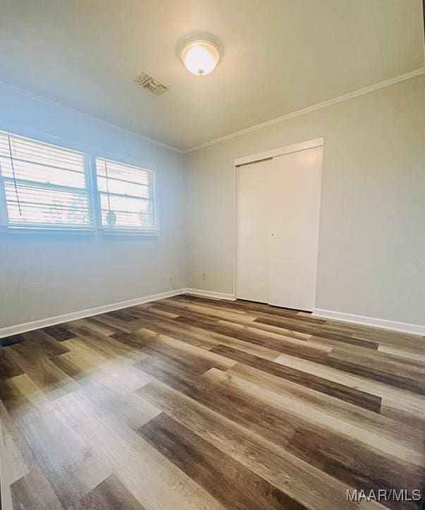 spare room with ornamental molding, wood finished floors, visible vents, and baseboards