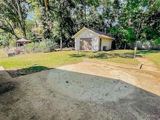 view of yard featuring an outdoor structure, a detached garage, a gazebo, and fence