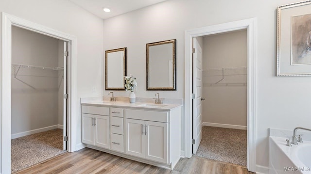full bath featuring double vanity, a sink, a bath, and wood finished floors