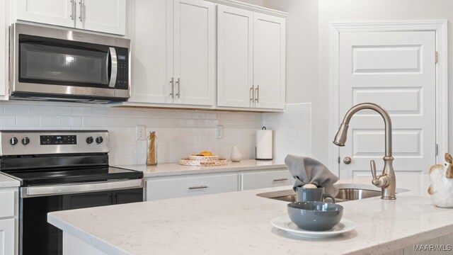 kitchen featuring stainless steel appliances, decorative backsplash, a sink, light stone counters, and white cabinets