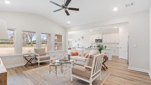 living room with light wood-type flooring, a ceiling fan, vaulted ceiling, and visible vents