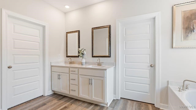 bathroom with a bath, double vanity, a sink, and wood finished floors