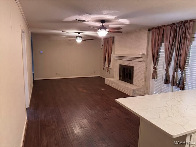 unfurnished living room with ceiling fan, dark wood-type flooring, visible vents, baseboards, and a brick fireplace