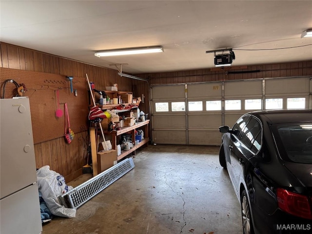 garage featuring a garage door opener, freestanding refrigerator, wooden walls, and a workshop area