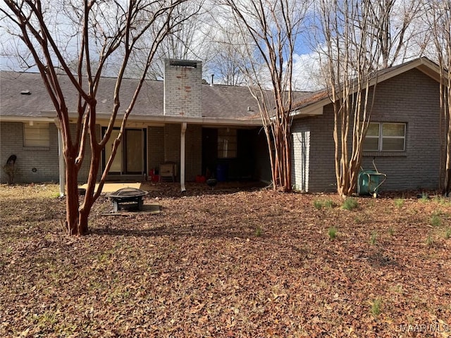 back of property featuring an outdoor fire pit, brick siding, and a chimney