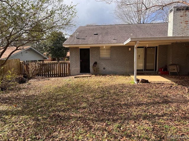 rear view of house featuring a shingled roof, a patio, a chimney, fence, and brick siding