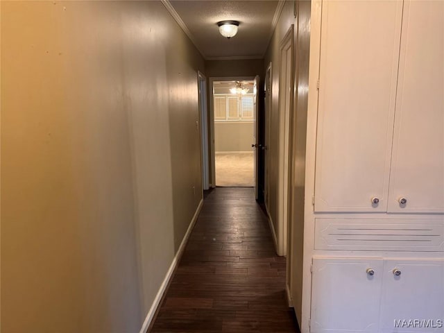 hallway featuring a textured ceiling, dark wood-type flooring, ornamental molding, and baseboards