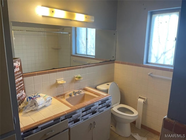 bathroom featuring a shower, toilet, a wainscoted wall, vanity, and tile walls