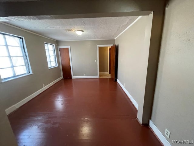 unfurnished room with dark wood-style flooring, visible vents, ornamental molding, a textured ceiling, and baseboards