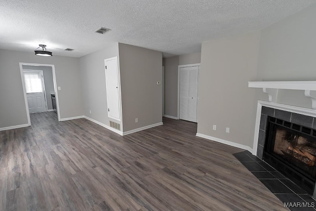 unfurnished living room featuring a tile fireplace, dark wood-style flooring, visible vents, and baseboards