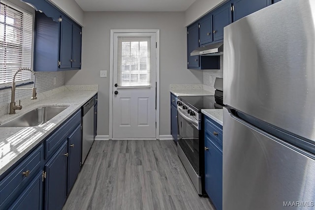 kitchen with blue cabinetry, stainless steel appliances, backsplash, a sink, and under cabinet range hood