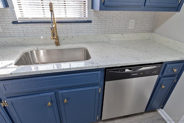 kitchen with stainless steel dishwasher, a sink, light stone counters, and blue cabinets