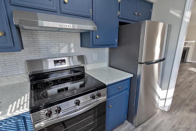 kitchen with blue cabinetry, under cabinet range hood, light stone counters, and stainless steel appliances