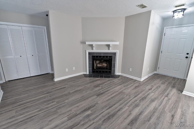 unfurnished living room featuring visible vents, a textured ceiling, wood finished floors, a tile fireplace, and baseboards