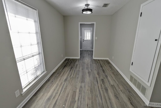 unfurnished dining area featuring a textured ceiling, dark wood finished floors, visible vents, and baseboards